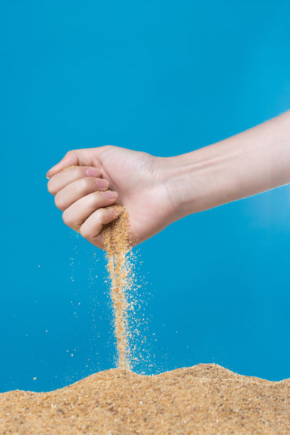 手释放掉沙。细沙在蓝色的背景下从手指间流淌。暑假海滩度假和时光流逝的概念。隔离式高速快门图片下载