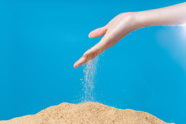 手释放掉沙。细沙在蓝色的背景下从手指间流淌。暑假海滩度假和时光流逝的概念。隔离式高速快门图片下载