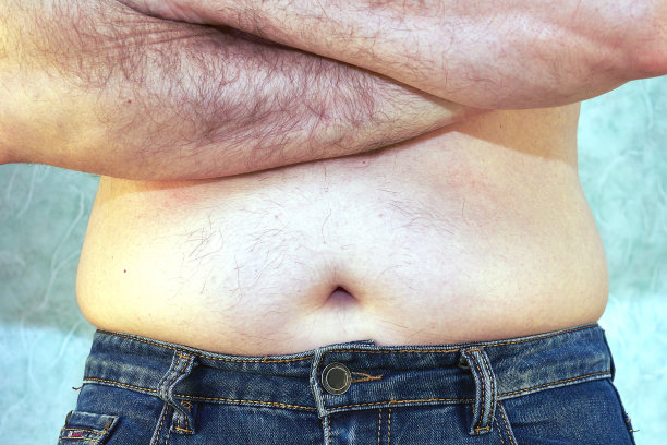 一个穿着牛仔裤的男人裸露着躯干和小肚子，特写了超重身体的正面概念图片下载