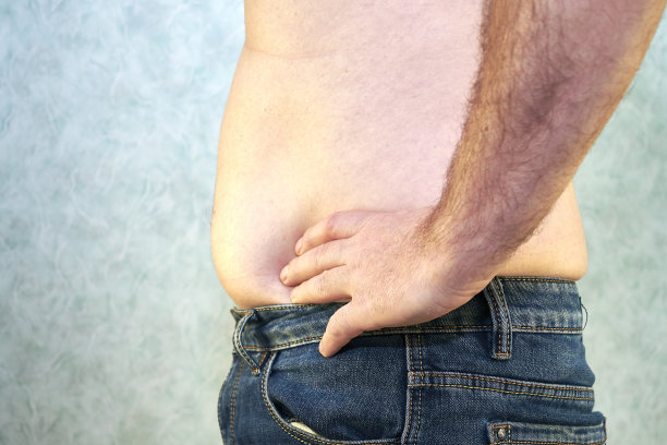 一个穿着牛仔裤的男人裸露着躯干和小肚子，特写了超重身体的正面概念图片下载