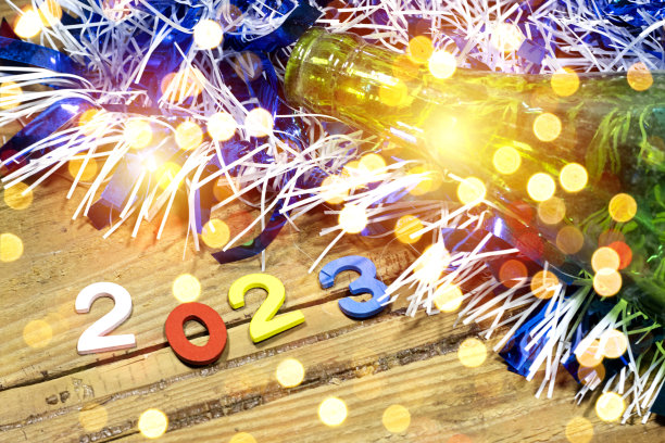2023年新年快乐背景新年节日卡片与明亮的灯光，金属箔和瓶子在木桌子上图片下载
