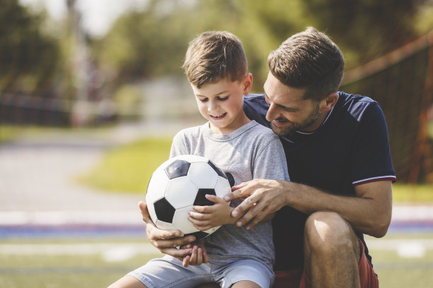 带着孩子的男人在球场外踢足球图片下载