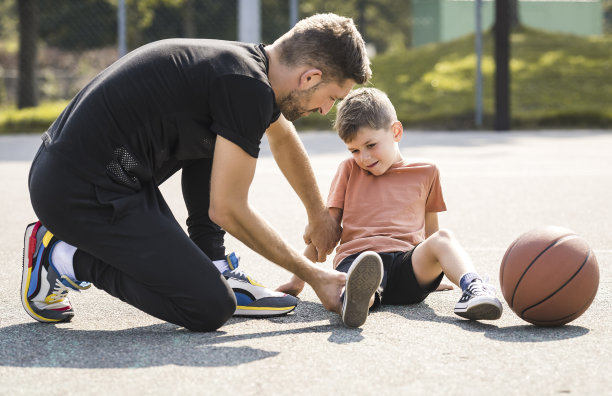 一名男子和一个小男孩在球场上打篮球，男孩脚踝受伤，哭了起来图片下载