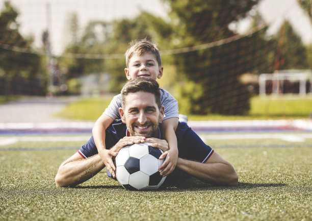 带着孩子的男人在球场外踢足球图片下载