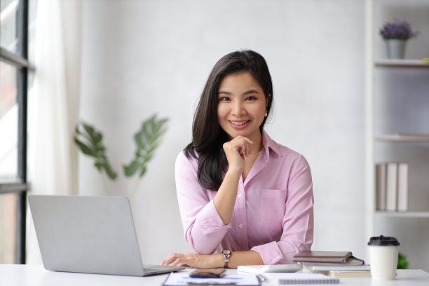 一个迷人的亚洲商业女性的肖像微笑着快乐地在家庭办公室的笔记本电脑上工作。图片下载