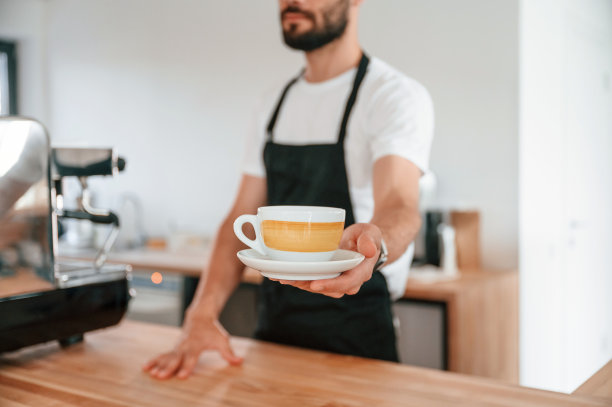 站着拿杯子。穿着白衬衫和黑围裙的咖啡馆工作人员在室内图片下载