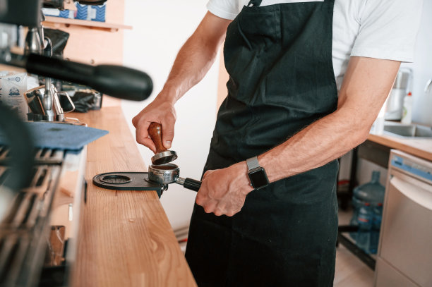 使用咖啡捣碎机。穿着白衬衫和黑围裙的咖啡馆工作人员在室内图片下载