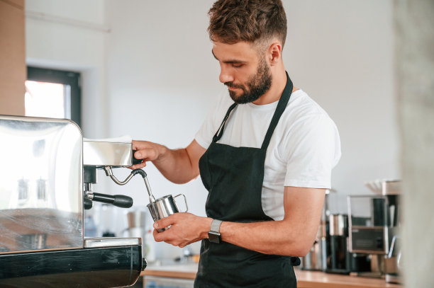 站着倒咖啡。穿着白衬衫和黑围裙的咖啡馆工作人员在室内图片下载