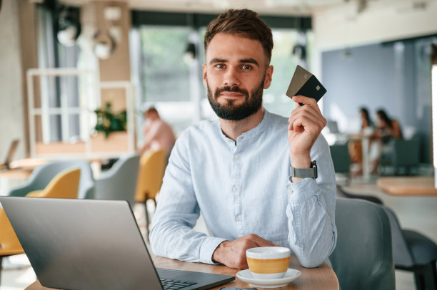 持有信用卡。一个年轻人正坐在咖啡馆里用笔记本电脑工作图片下载