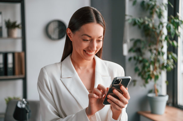 使用智能手机。年轻貌美的女士穿着正装正在办公室工作图片下载