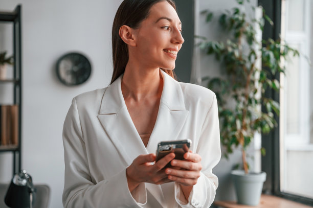 使用智能手机。年轻貌美的女士穿着正装正在办公室工作图片下载