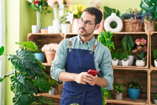 年轻的西班牙男子在花店用智能手机微笑自信图片下载