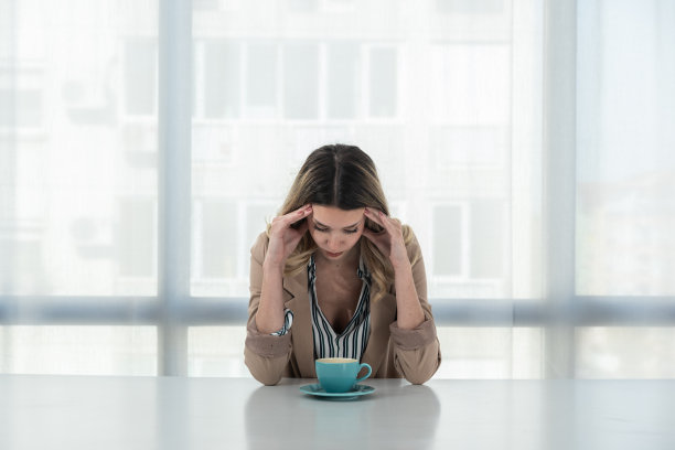 但先喝杯咖啡。年轻的不快乐的疲倦的穿着正式的商业妇女坐在办公室的空桌子上一杯咖啡。女性白领，自由职业者金融专家早上例行公事。图片下载