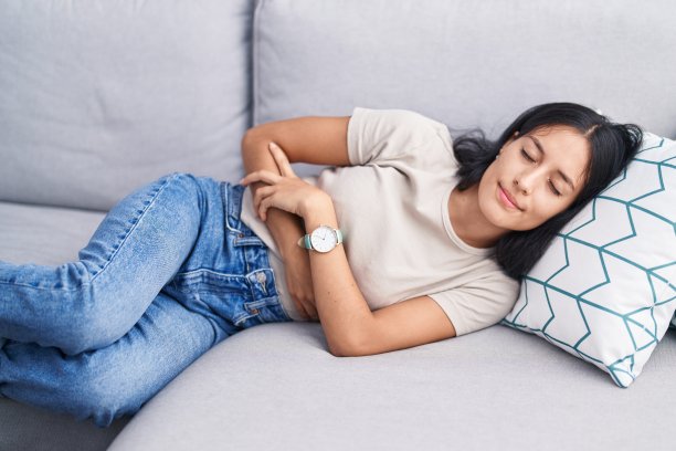 年轻美丽的西班牙妇女忍受胃痛躺在家里的沙发上图片下载