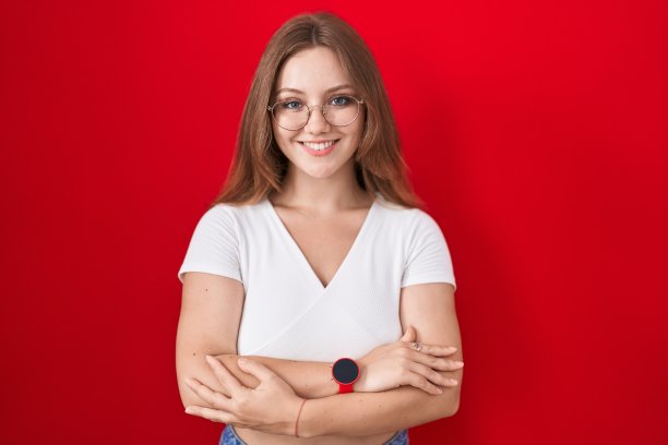 年轻的白人妇女站在红色背景快乐的脸微笑，交叉双臂看着相机。积极的人。图片下载