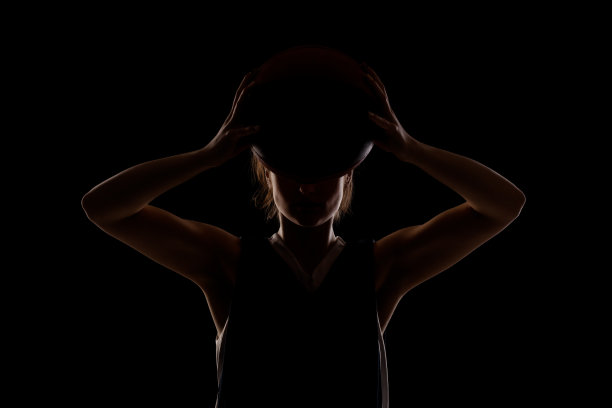 女篮球运动员。漂亮的女孩把球举在面前。侧光剪影工作室肖像对黑色背景..图片下载