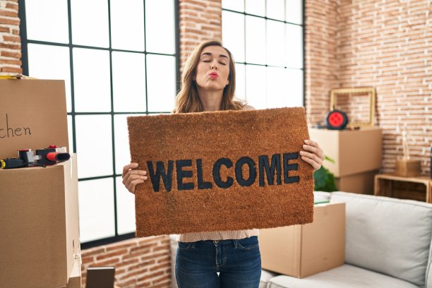 年轻女子在新家抱着欢迎的门垫，看着镜头飞吻，可爱又性感。爱的表达。图片下载
