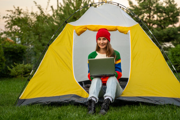 一名年轻女子正悠闲地坐在旅游帐篷里，用笔记本电脑工作。远程工作和亲近自然的概念图片下载