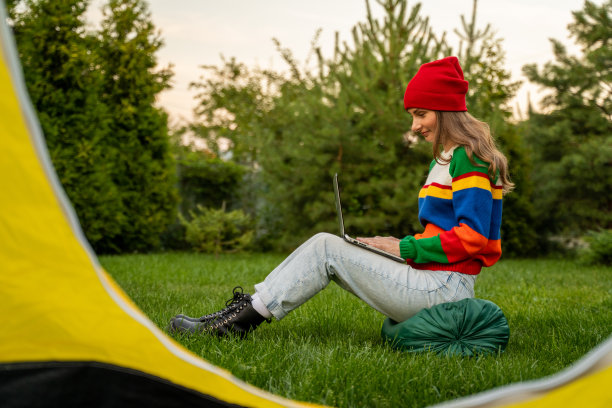 在户外被美丽的大自然包围的露营帐篷附近，一名妇女正在使用笔记本电脑图片下载