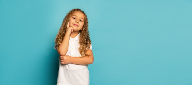 微笑的孩子。可爱的小女孩，长卷头发的孩子看着相机孤立在蓝色背景。观念儿童积极的情绪、美好的事物图片下载