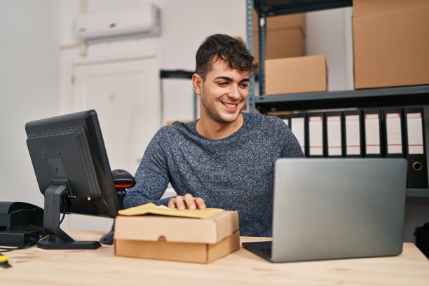 年轻的西班牙人电子商务工作人员使用笔记本电脑在办公室拿着包裹图片下载