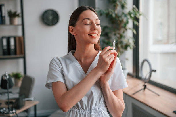 站着拿着注射器。穿着白大褂的年轻漂亮的女医生在办公室图片下载