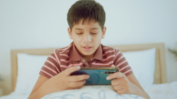 一个印度年轻人在家里玩智能手机游戏。图片下载