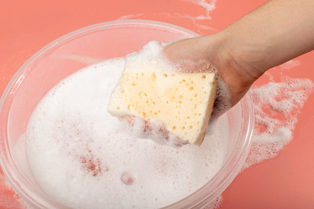 一个盆与肥皂水，手持肥皂海绵与泡沫在粉红色的背景图片下载
