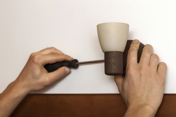 修理工用螺丝刀将灯固定在墙上。图片下载