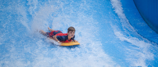 一个小男孩在水上公园的游泳板上冲浪的特写图片下载
