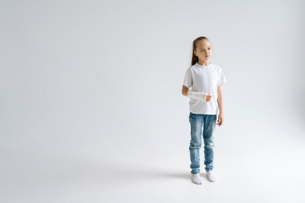 完整的肖像甜美的小女孩破碎的手包裹在白色石膏绷带站在白色孤立的背景，看向远方。图片下载