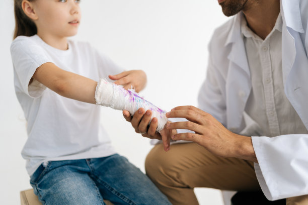 特写裁剪的镜头，无法辨认的男性医生在制服咨询小女孩病人骨折的手包裹在石膏绷带。图片下载