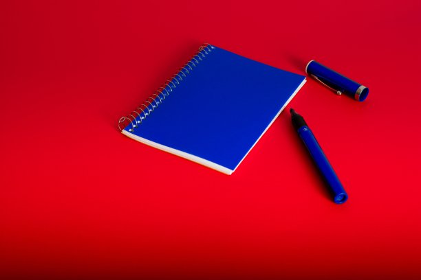 红色背景的蓝色螺旋装订记事本钢笔图片下载