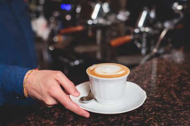 咖啡师在咖啡屋酒吧的咖啡机前工作，调酒师在制作卡布奇诺或拿铁，调酒师在咖啡馆柜台准备咖啡饮料图片下载