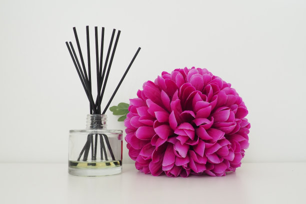 在白色的房间里，用香烛、香精油装在一个玻璃花瓶里，用鲜亮的粉色丁香毛圈人造花装饰。白色背景图片下载
