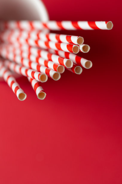 红色背景上杯中的红白条纹吸管特写图片下载