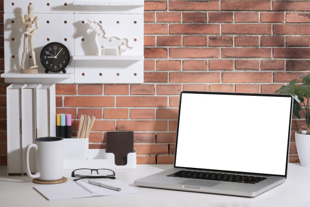 笔记本电脑，书，咖啡杯和盆栽在白色的砖墙桌子上。创造性的工作。图片下载