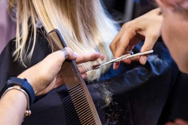 近距离发型师为可爱的金发小女孩在发廊做时髦的发型。女理发师在理发店为婴儿做发型。发型，美的概念。本空间图片下载