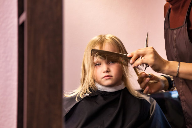 美发师妇女在发廊为可爱的金发小女孩做时髦的发型。理发师在理发店为婴儿做有风格的发型。发型，美的概念。本空间图片下载