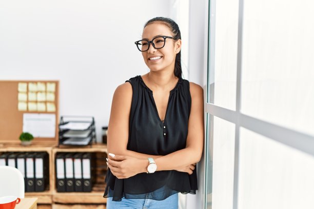 年轻的拉丁妇女微笑着，自信地站在办公室，双臂交叉图片下载