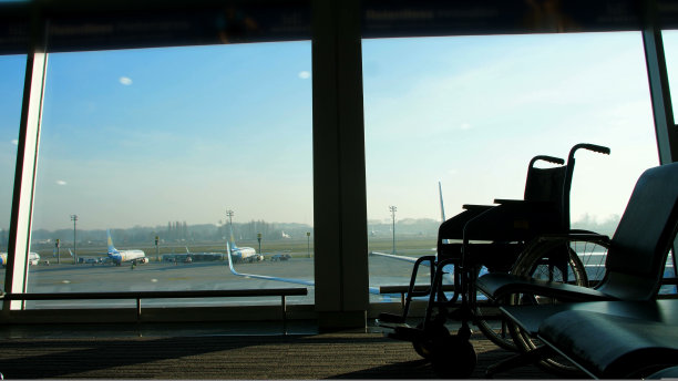 在机场的候机室里，对着窗外的背景俯瞰着飞机和跑道，是一个轮椅，你可以看到它的轮廓。图片下载