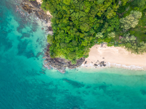 从上到下俯瞰的热带海滩，蓝绿色的海水，白色的沙子和巨大的岩石。岩石上生长着树木和棕榈树。热带的主题。图片下载