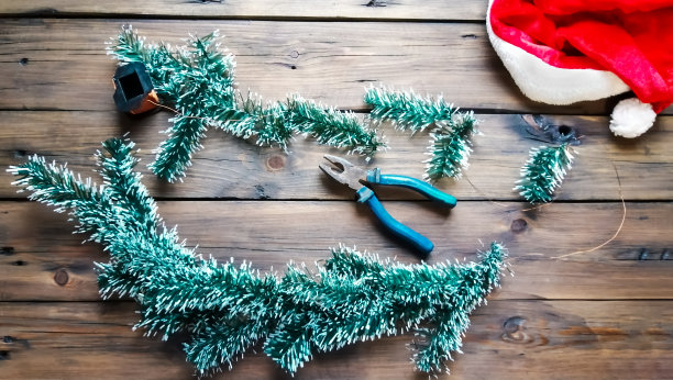 木桌上放着云杉树枝、钳子和钓鱼线，用来做花环。制作圣诞树花环的过程。为新年和圣诞节准备的云杉树枝花环。图片下载