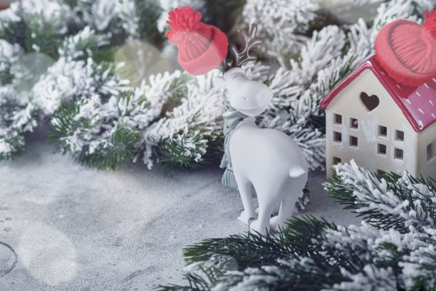 新年贺卡。圣诞节。两栋房子用白色围巾包裹着，圣诞树的树枝在雪里，有趣的驯鹿和美丽的散景。新年静物。节日气氛的圣诞节。图片下载
