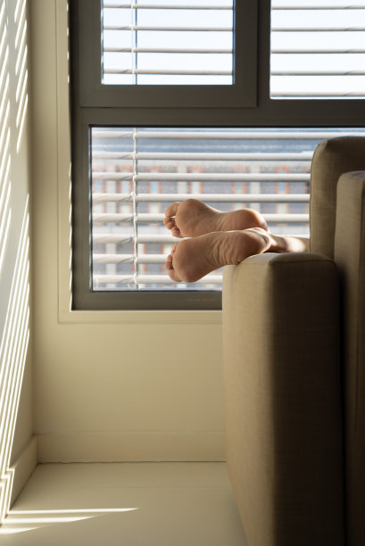 男人光着脚坐在沙发上，背景是一扇窗户。图片下载