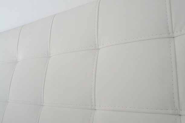 柔软的床头板。真皮:用真皮或人造皮革和织物制成的家具的内饰柔软的床头板靠在浅色的墙上。图片下载