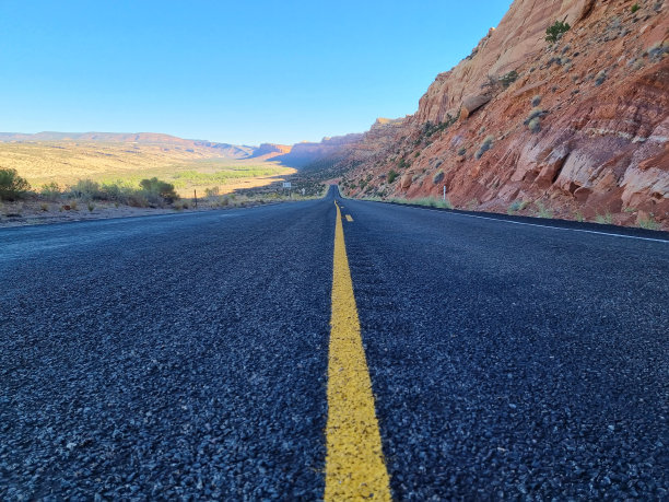 沙漠中废弃的黑色沥青路，周围是红色的砂岩岩层图片下载