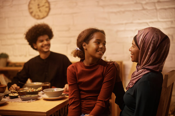 快乐的穆斯林小女孩在餐桌上和她的妈妈说话。图片下载