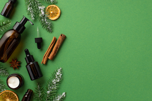 冬季季节性护肤理念。俯视图照片泵滴管瓶奶油罐松枝在霜茴香肉桂棒和干橙片孤立的绿色背景与空白图片下载