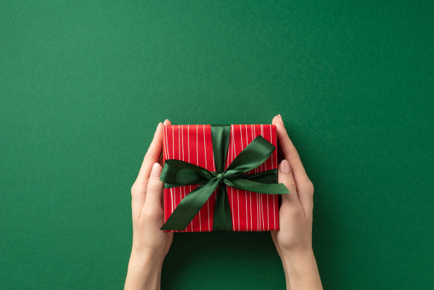 新年的概念。第一人称俯视图照片的妇女的手给红色的礼物盒与丝带蝴蝶结孤立的绿色背景与空白图片下载
